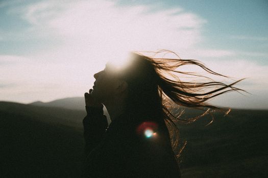 Silhouette of a woman with long hair blowing in the wind, against a backlit sunset sky in Koktebel.