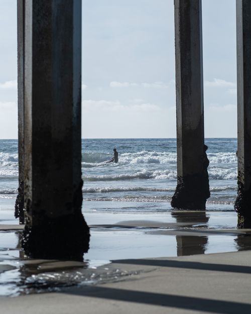 Free A surfer rides the waves beneath a pier at Ocean Beach, San Diego. Stock Photo
