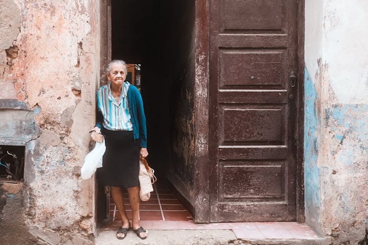 An Elderly Woman Standing On The Doorway