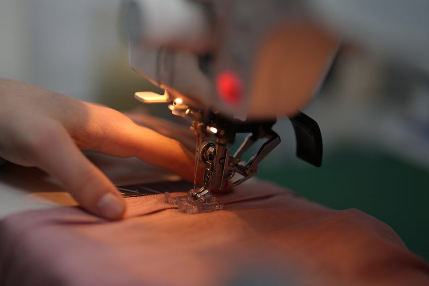 Hands guiding fabric beneath a sewing machine needle to mend or make a garment