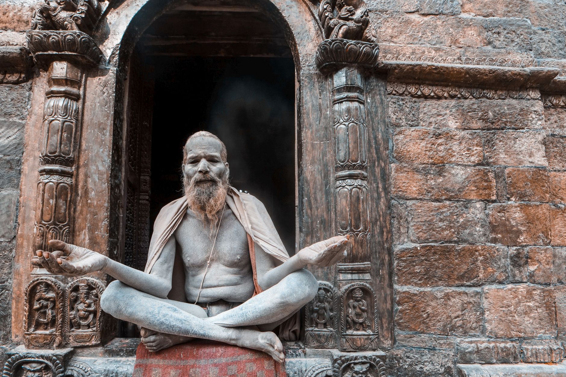 A bearded monk meditates cross-legged at the entrance of an ancient temple, evoking a serene spiritual atmosphere.