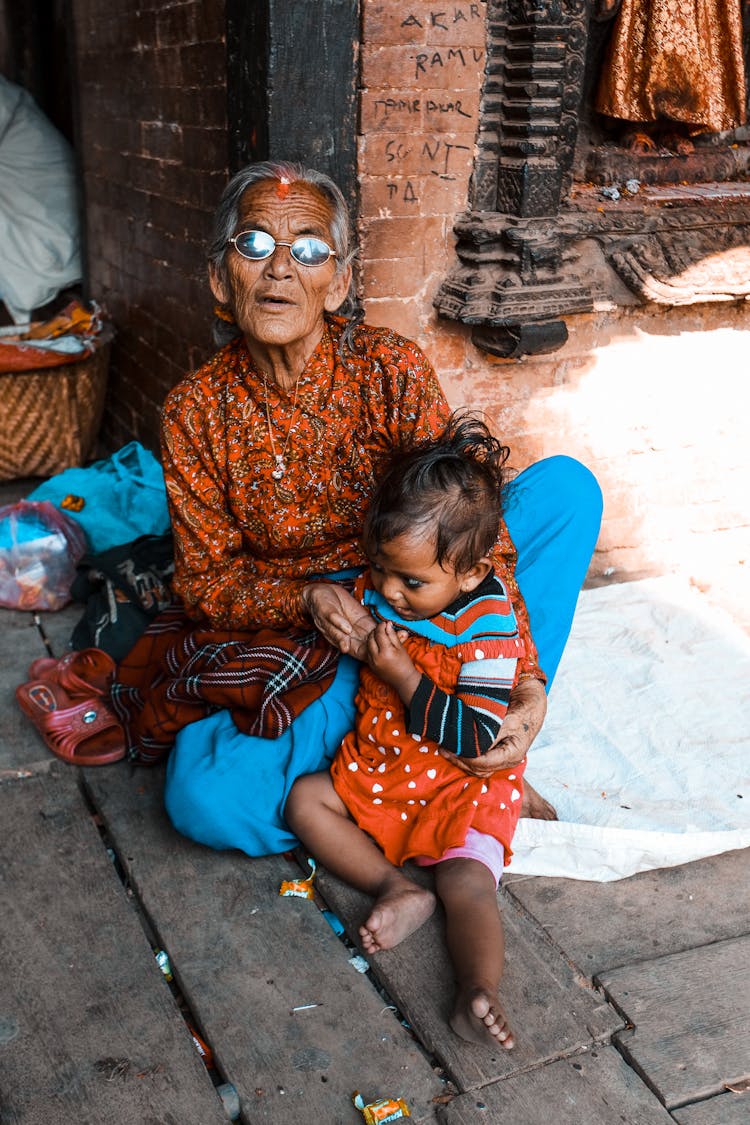 An Elderly Woman Sitting On The Ground With A Child