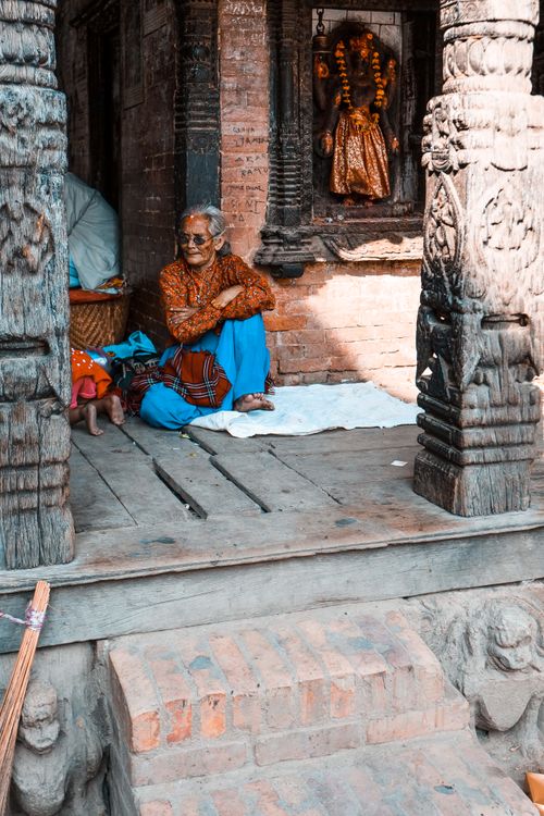 Free An elderly woman sitting calmly on traditional temple steps in Nepal, showcasing local culture. Stock Photo
