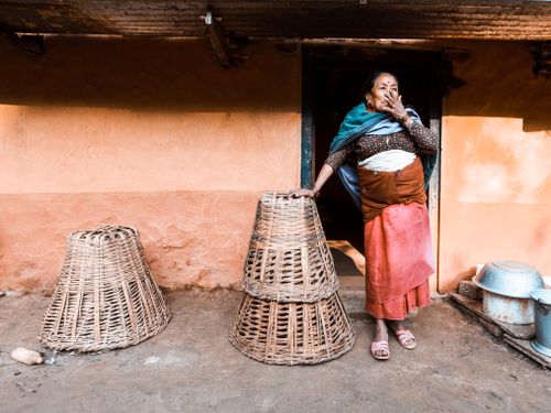 Free Senior woman in traditional clothing with woven baskets outside a rural home, showcasing cultural heritage. Stock Photo