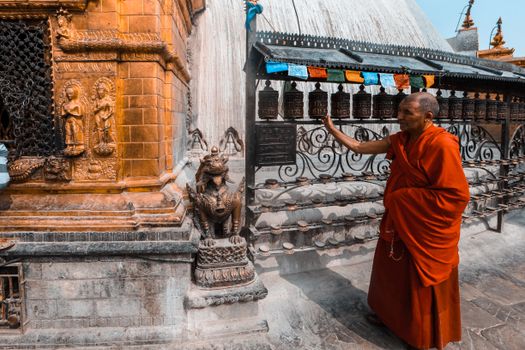Monk in red robes walking past intricate Buddhist temple carvings and prayer wheels.
