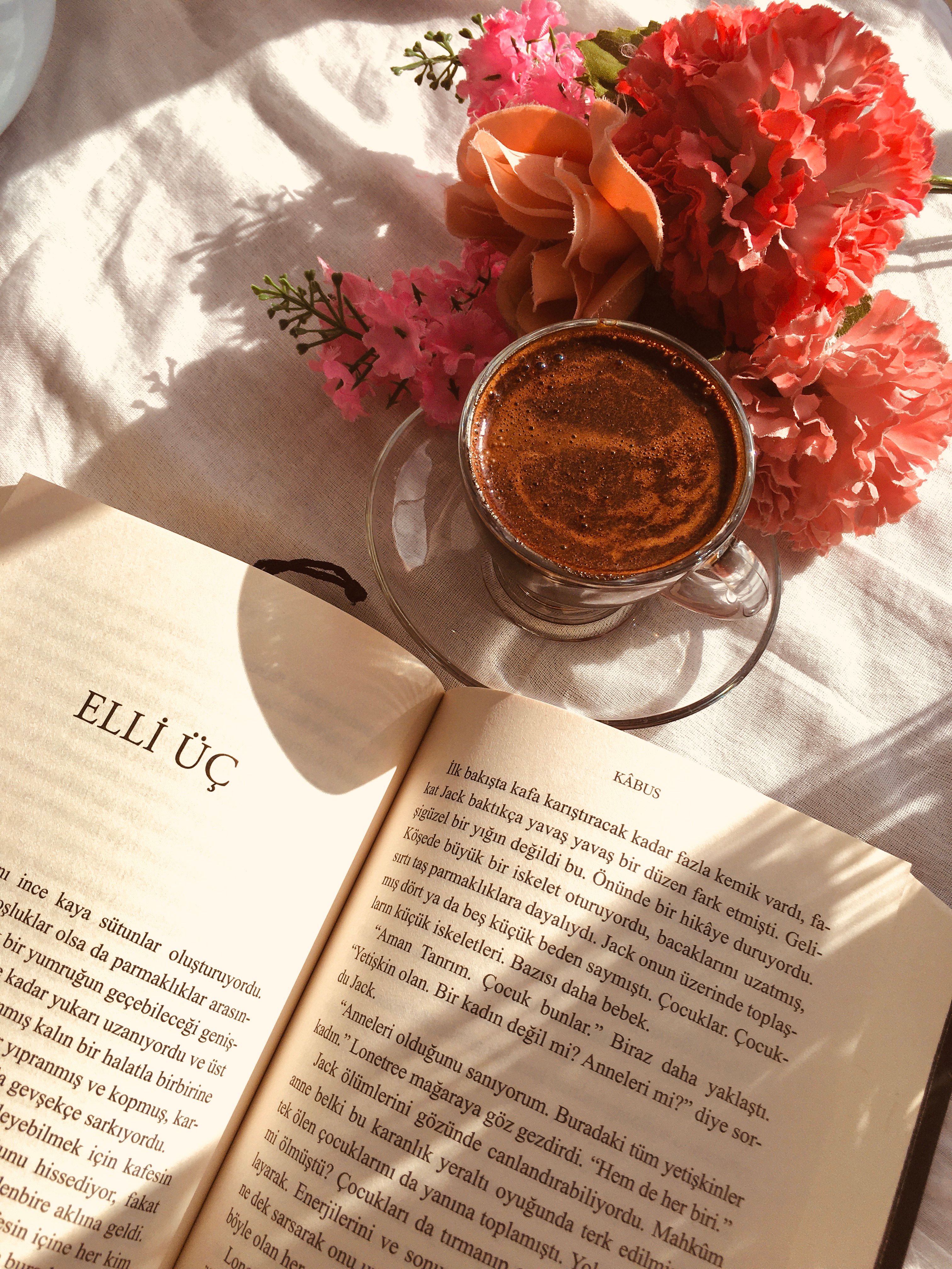 A cozy scene featuring a cup of coffee, an open book, and vibrant flowers on a sunlit surface.