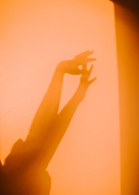 Shadow of hands on a warm orange wall capturing light and movement in an abstract artistic composition.