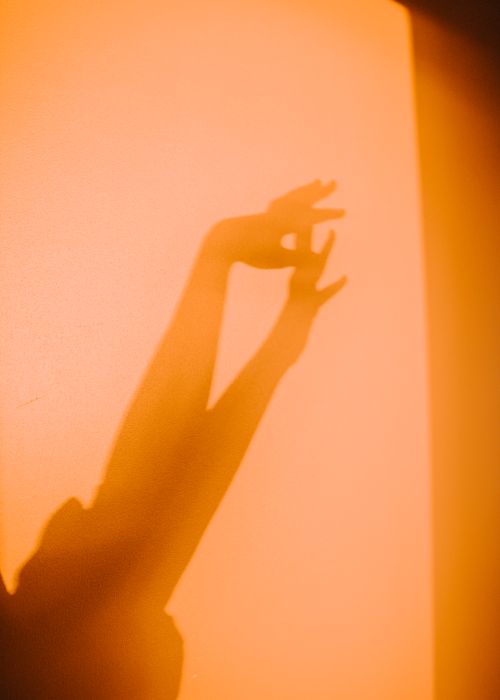 Free Shadow of hands on a warm orange wall capturing light and movement in an abstract artistic composition. Stock Photo
