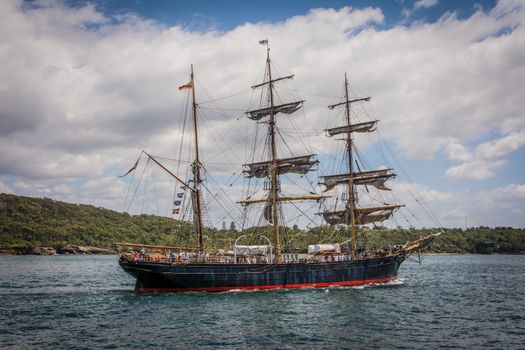 A majestic tall ship sails across the scenic Sydney Harbor, Australia, under clear blue skies.