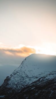 Dramatic snow-covered mountain peak in Norway, glowing under a beautiful sunset sky.