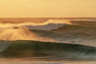 日落时分，戏剧性的海浪袭来，冲浪者接住了海浪