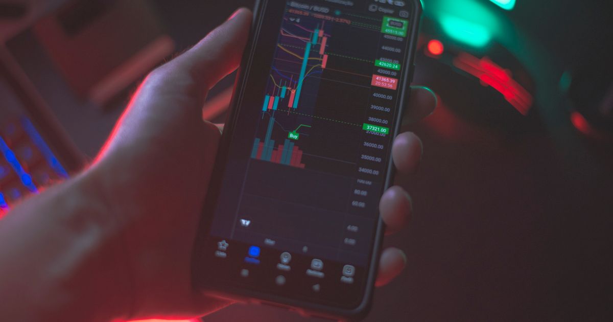 Mão segurando smartphone exibindo aplicativo de negociação de criptomoedas com dados financeiros.