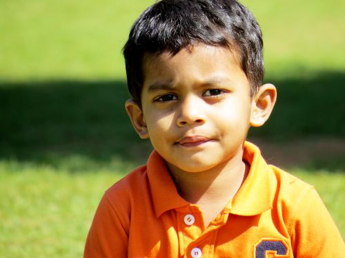 Free Close-up portrait of a young boy outdoors in a bright orange polo shirt with lush green background. Stock Photo