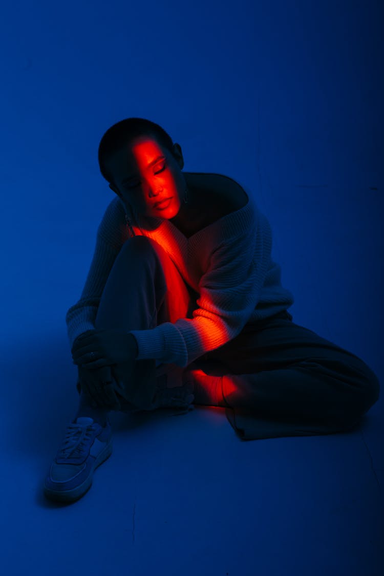 Young Woman Sitting On Floor In Stripe Of Red Light In Dark Room 