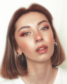 Close-up portrait of a woman with striking red eye makeup and a confident gaze.