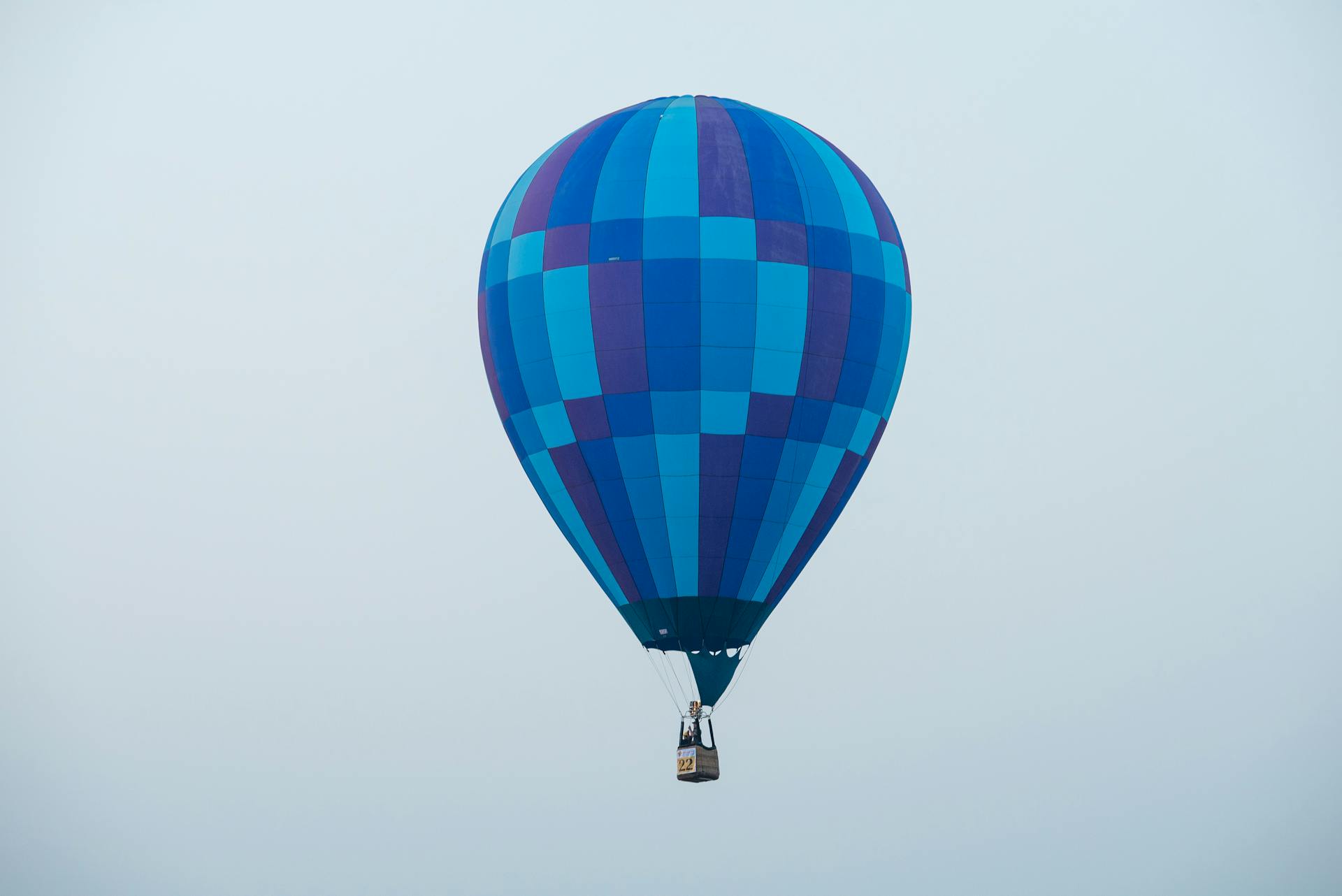 A vibrant blue hot air balloon with a colorful pattern floats elegantly against a clear sky.