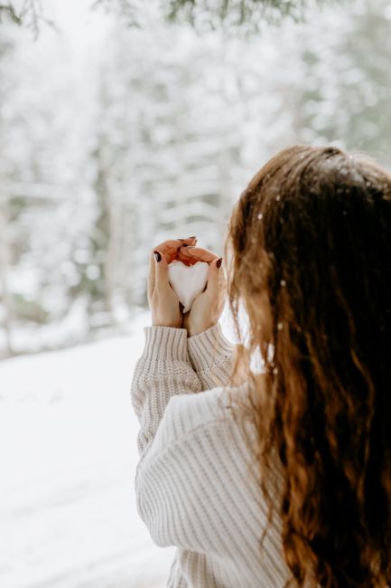 A woman with long hair holds heart-shaped snow in a snowy forest, capturing the essence of winter.