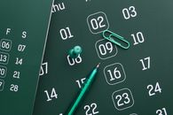 Close-up of a green calendar with pen, push pin, and paper clip for planning and organization.