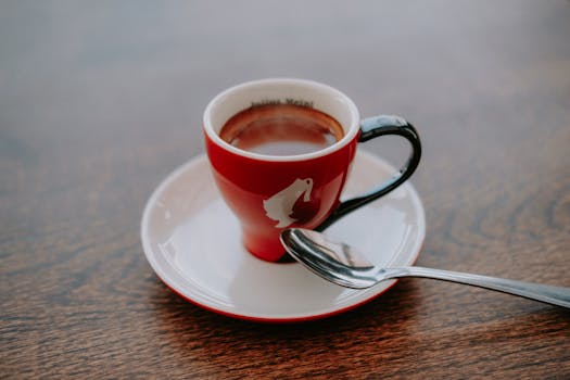 Steaming coffee served in a red cup with saucer and spoon on a wooden table.