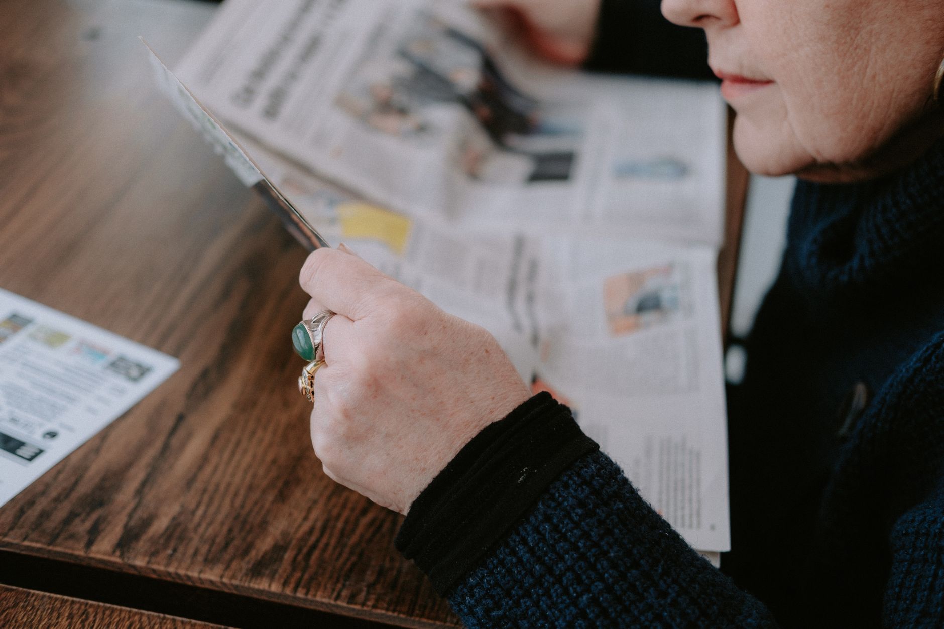 A woman reads a newspaper at a wooden table, focusing on leisure and information.