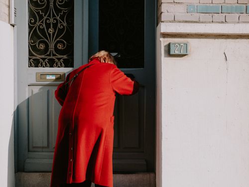 Free A person in a red coat enters a distinctive blue door with ornate decoration. Stock Photo