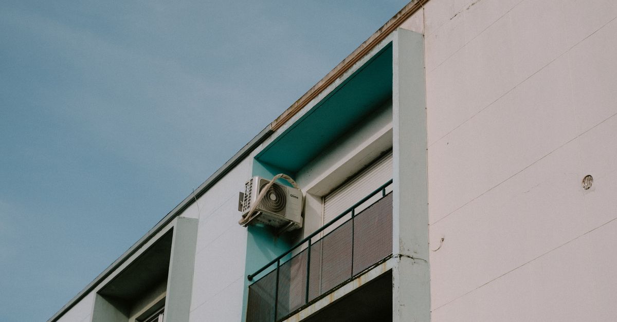 A low angle view of a modern apartment building featuring a balcony and air conditioner unit.