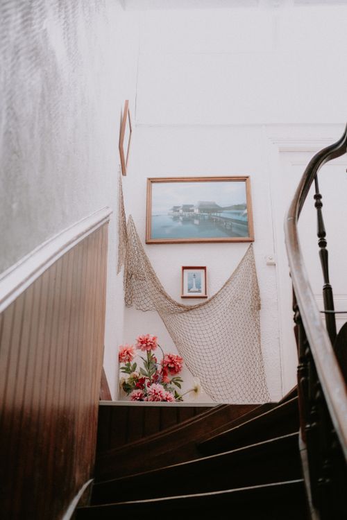 Free Elegant staircase with hanging art and floral arrangement, creating a cozy home ambiance. Stock Photo