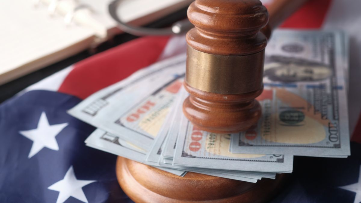 A judge's gavel resting on US dollar bills in front of an American flag