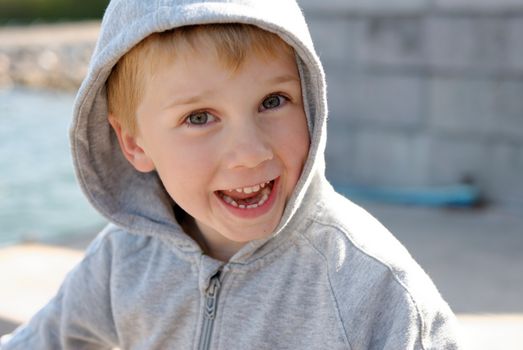 A smiling young boy enjoying a sunny day outdoors in his grey hoodie.
