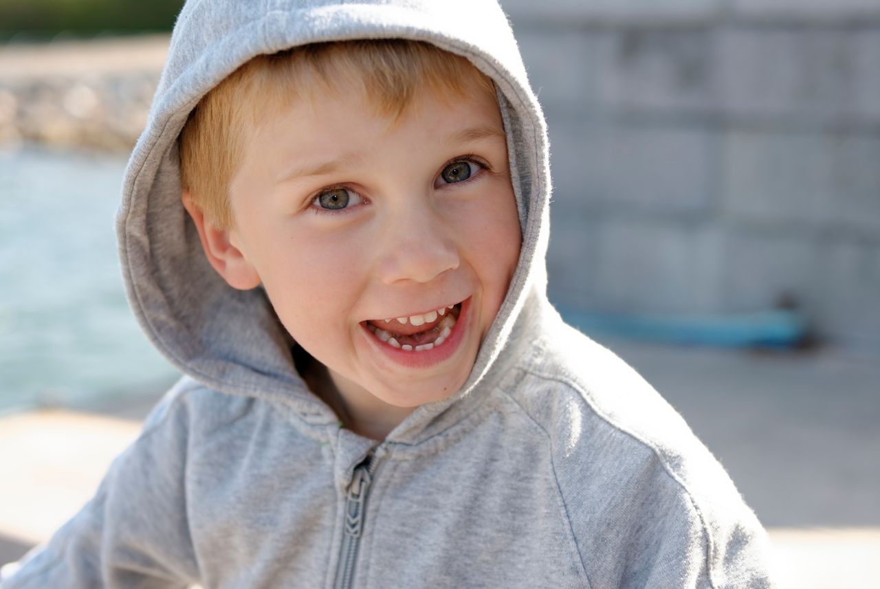 a smiling young boy enjoying a sunny day outdoors in his grey hoodie