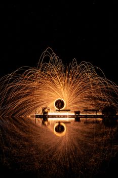 A captivating steel wool light painting creates fiery sparks over water.