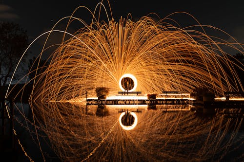 Steel Wool Photography of Man Standing on Dock during Night Time