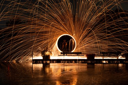 Man performing steel wool spinning, creating stunning light trails at night.