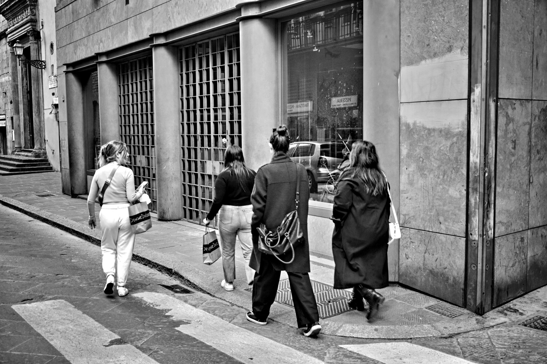 Four women walking along a city street in a black and white setting, showcasing urban life.