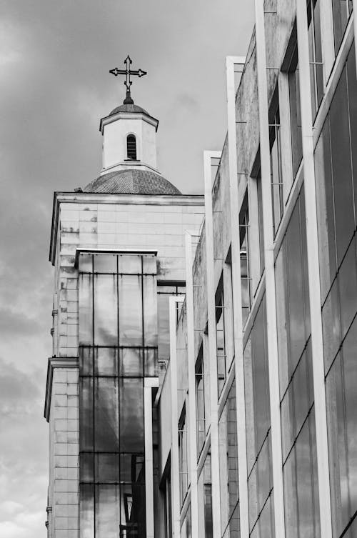Grayscale Photo of Concrete Building beside a Church Tower 