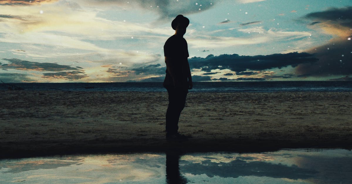 A solitary figure silhouetted against a twilight beach scene with stars and reflection.
