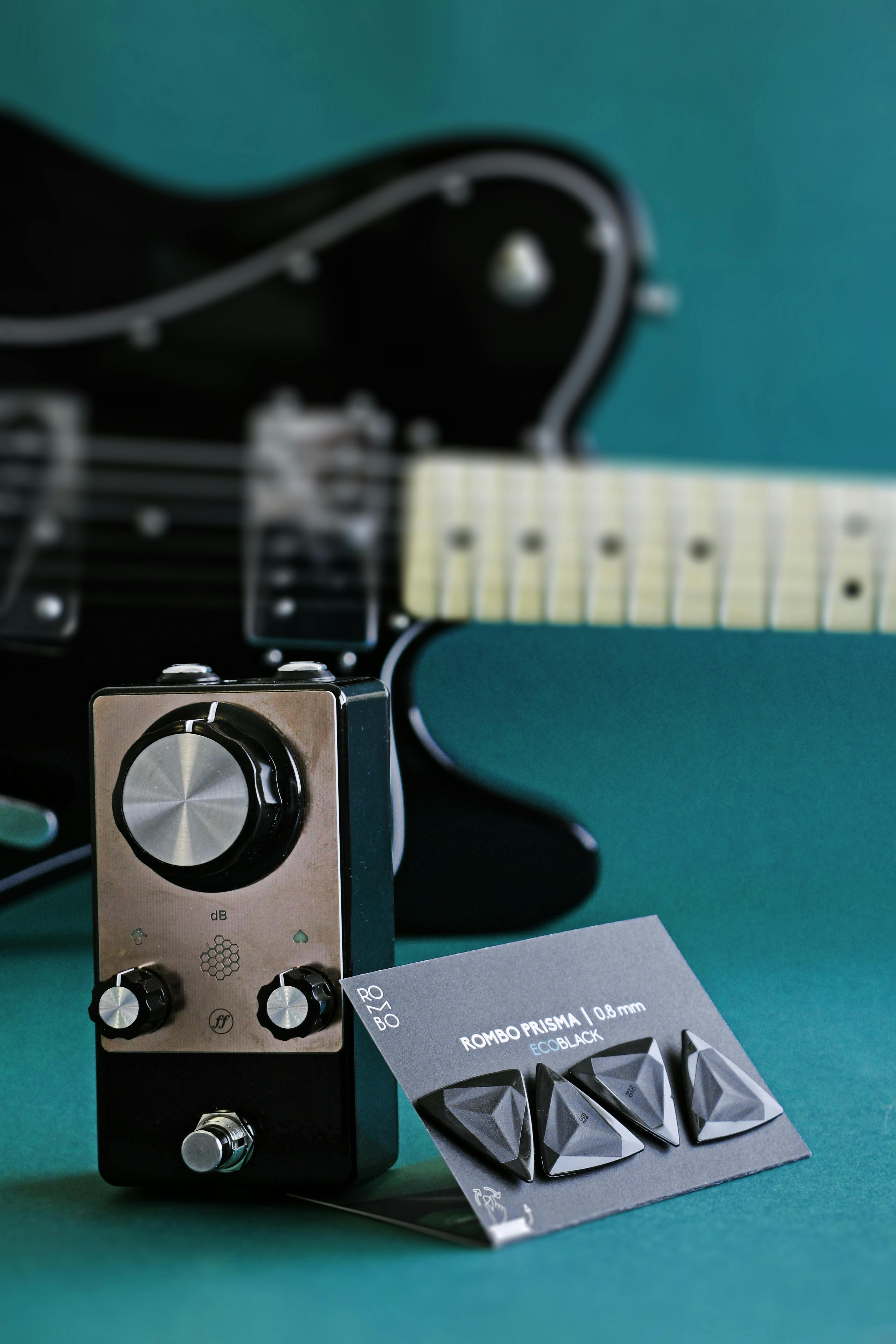 Close-up of guitar pedal and picks with a blurred electric guitar background.