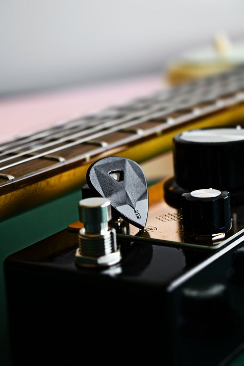 Free Detailed image of an electric guitar with a pick, knobs, and strings in focus. Stock Photo