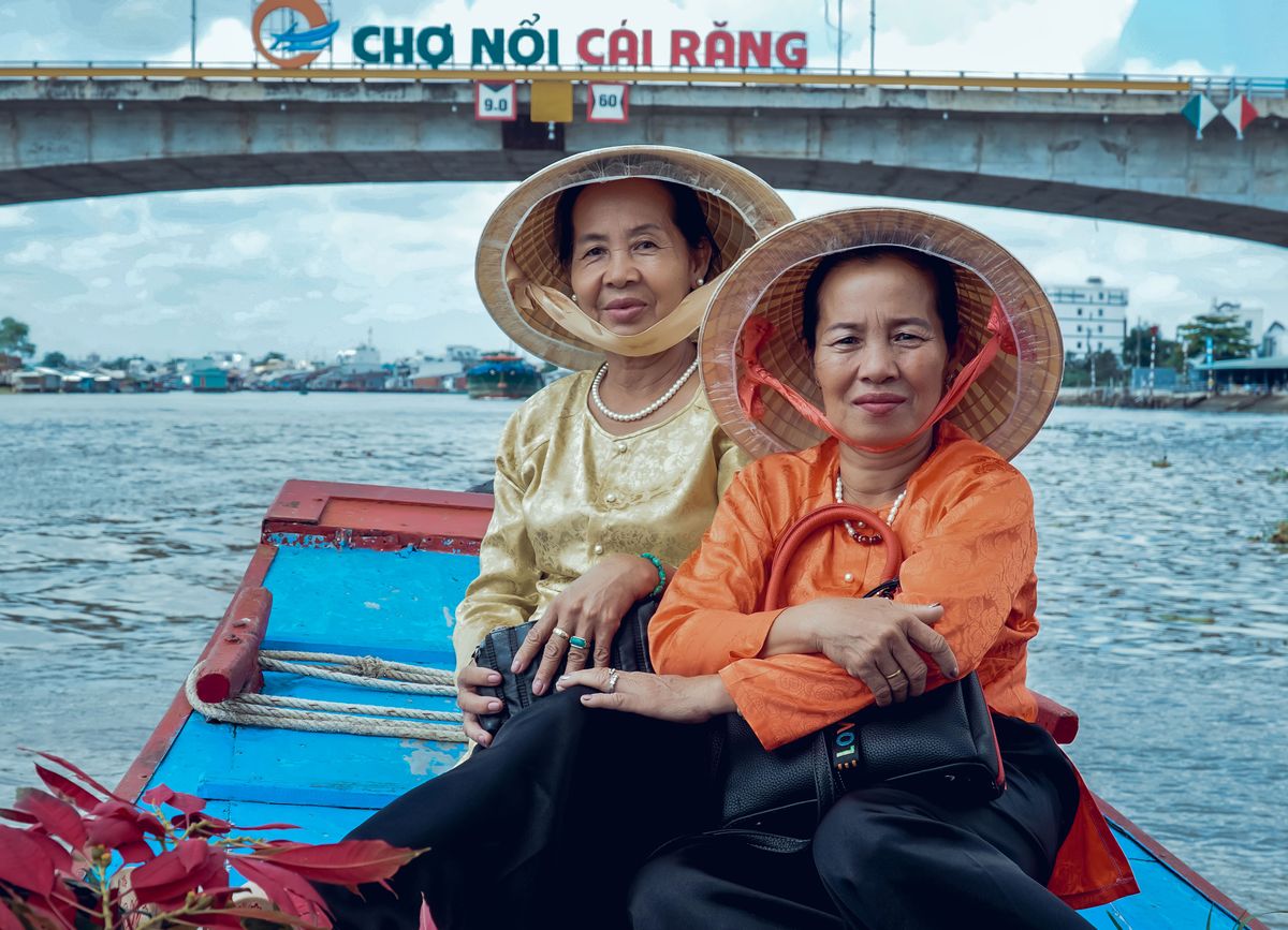 Two women sitting on a boat near the Cai Rang floating-market sign