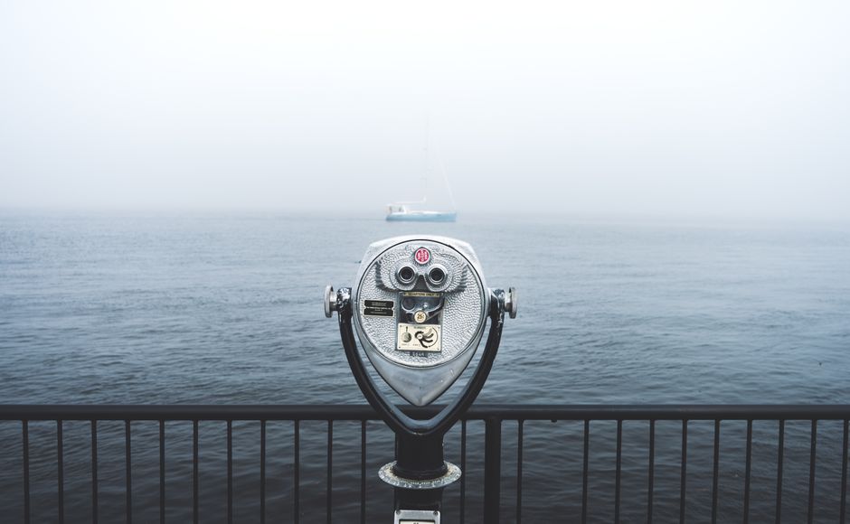 A foggy ocean view with a pair of binoculars and distant sailboat.