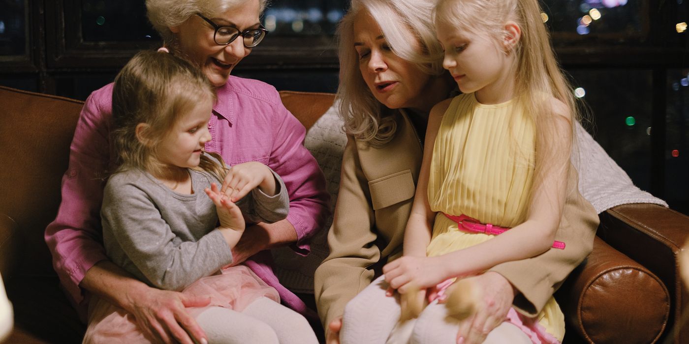 A warm family moment indoors with two grandmothers and two granddaughters sitting together on a sofa.
