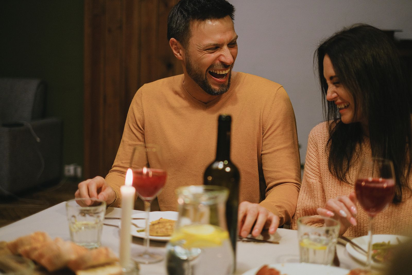 A couple laughing together over a warm drink at home