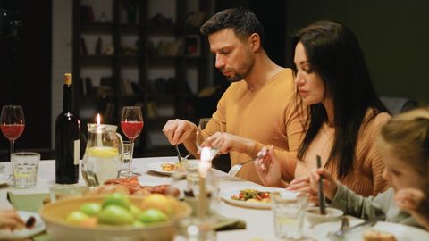 A family gathered around a dinner table indoors, enjoying a meal together with wine and candles.