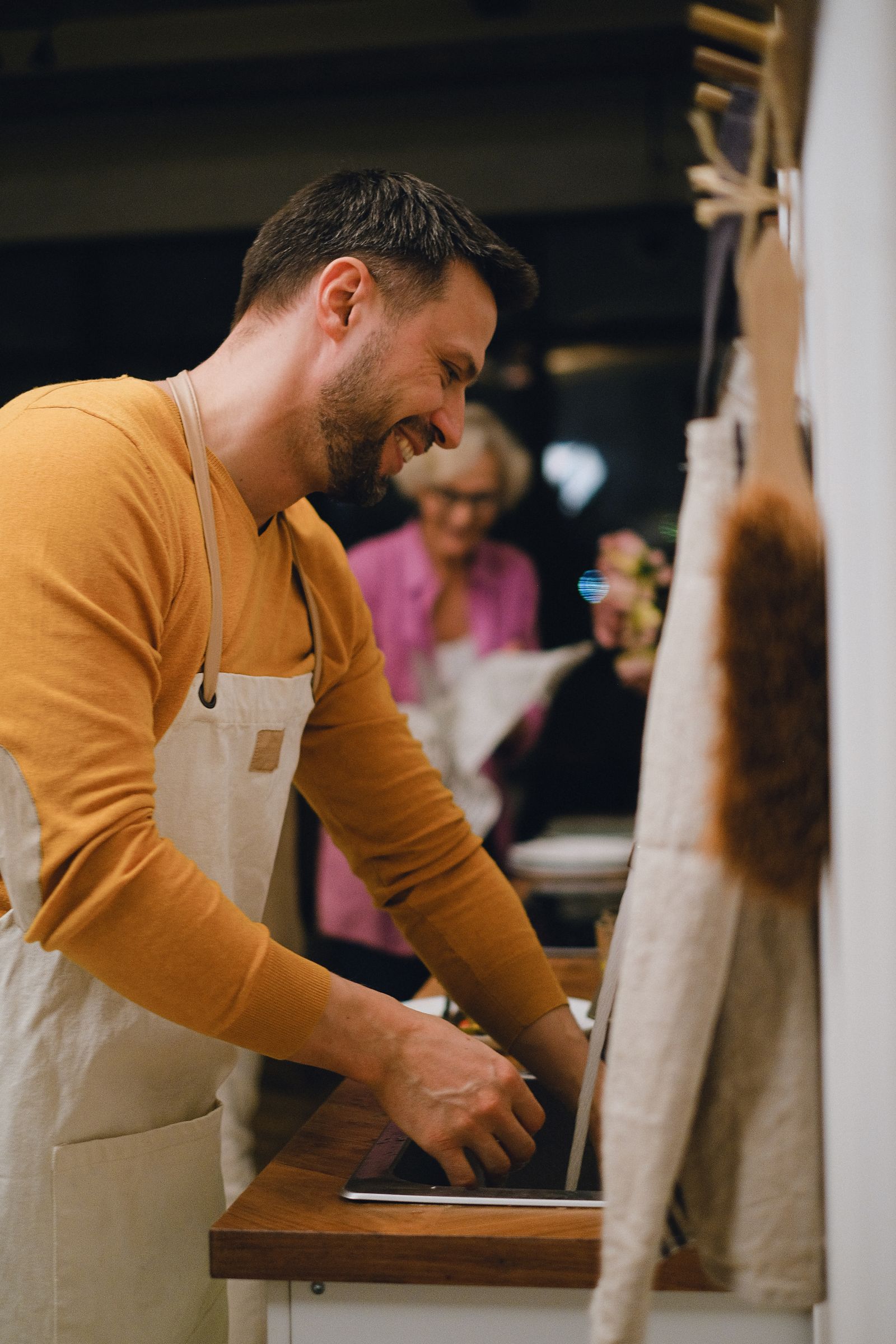 A smiling bearded man in an apron washing up at a kitchen sink