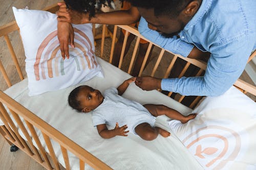 Free A Parent Holding Hands with a Baby in a Crib Stock Photo