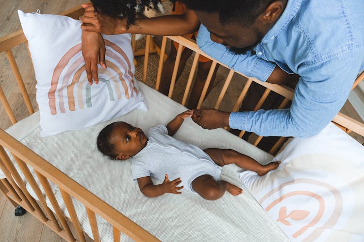 A Parent Holding Hands With A Baby In A Crib