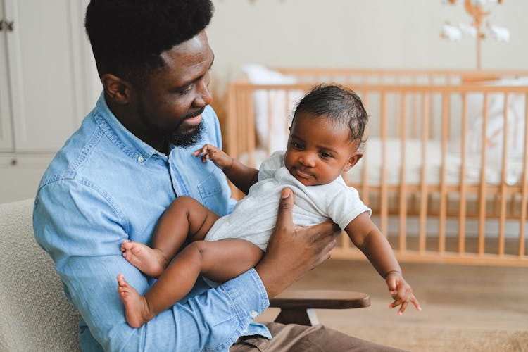 Man In Denim Shirt Carrying Baby In White Ones