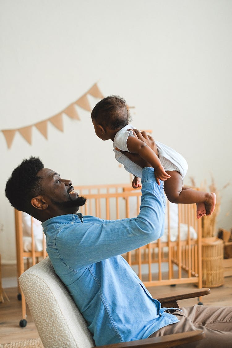 A Man In Blue Long Sleeve Shirt Lifting A Baby