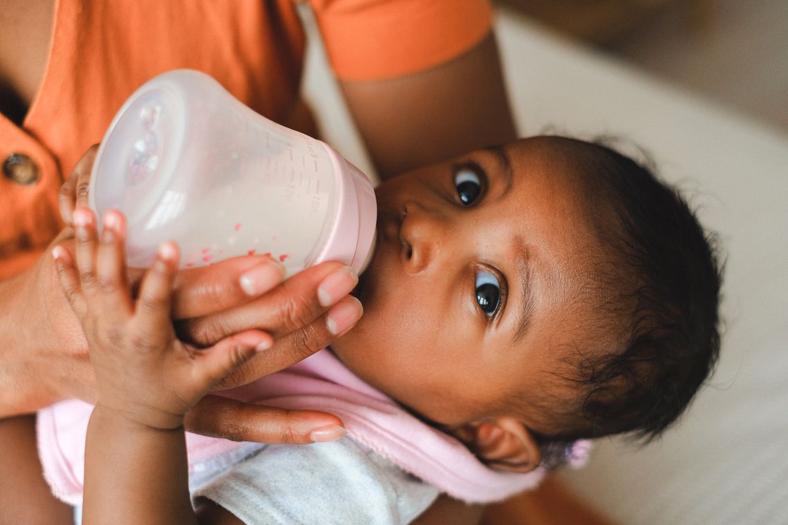 Baby drinking milk from a bottle while being held by a caregiver