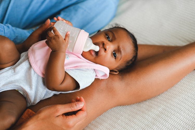 A Baby Drinking Milk While Lying Down On Persons Legs